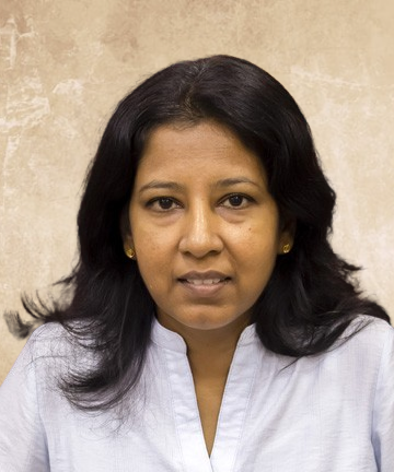 Head-and-shoulders portrait of a woman with dark hair and a light blue blouse, neutral expression, standing against a beige textured background.