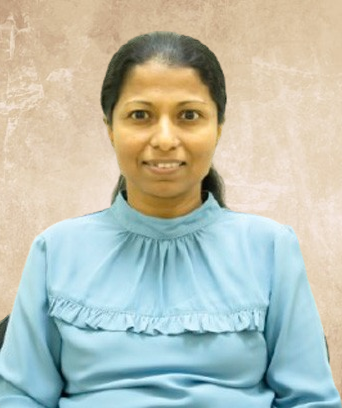 Portrait of a woman with dark hair tied back, wearing a light blue blouse, smiling at the camera against a beige background.